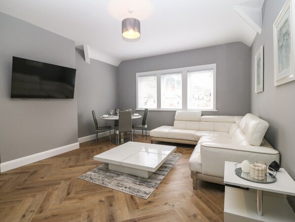 A modern living room with a flat-screen TV, a white sofa, a dining table with chairs, and a coffee table. - Park View Upper, in Llandudno. (Llandudno)