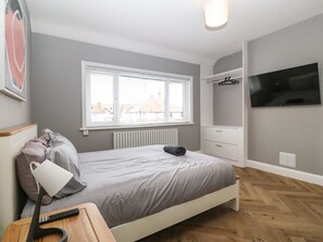 A bedroom with a bed, bedside lamp, window, radiator, TV, and a wardrobe. - Park View Upper, in Llandudno. (Llandudno)
