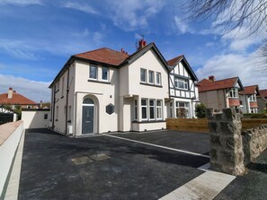A two-story house with a driveway, a stone wall, and a clear sky. - Park View Upper, in Llandudno. (Llandudno)