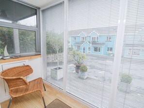 Ein Zimmer mit einem großen Fenster, einem Korbstuhl und Blick auf ein blaues Gebäude.
