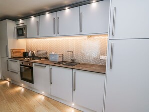 Eine moderne Küche mit Edelstahlgeräten, einer Fischgräten-Fliesenrückwand und einer Holz Arbeitsplatte.
