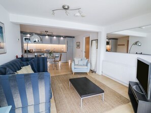 Ein modernes Wohnzimmer mit Sofa, Couchtisch, Fernseher und einer Küche im Hintergrund.