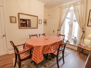 A dining room with a round table, six chairs, a checkered tablecloth, a mirror, and a window with curtains.