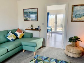 A living room with a green sofa, a patterned rug, and a small table with a bottle and glasses. - 2 Boathouse Terrace in St Eval (Wadebridge)