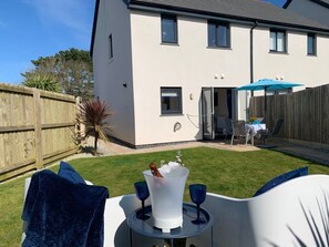 A house with a white exterior, a wooden fence, and a backyard with a table and chairs. - 2 Boathouse Terrace in St Eval (Wadebridge)