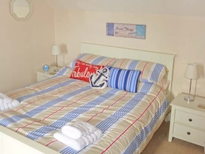 Una cama bien tendida con ropa de cama a rayas, un cojín con un diseño de ancla náutica y un letrero en la pared.