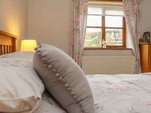 A bed with floral bedding, a lamp, and a window with curtains. - Jack's Nest, South Molton (South Molton)