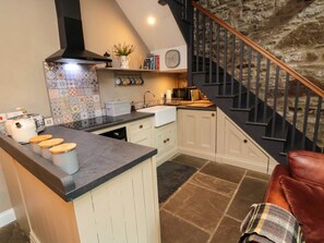 Une cuisine avec un sol en pierre, un escalier noir et un fauteuil en cuir marron.