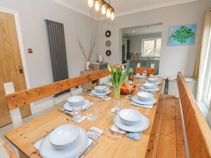 A dining area with a long wooden table set for a meal, a radiator, and a kitchen in the background. - Morningside, Totland Bay. WiFi (Totland Bay)
