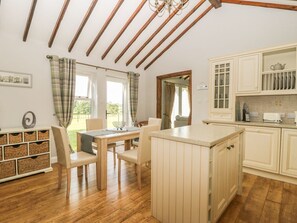 A kitchen with wooden cabinets, a dining area with a table and chairs, and a view of the outdoors. - The Barn at Orchard Farm, York (York)