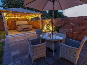 An outdoor patio with wicker furniture, a glass table, and a barbecue area with string lights.