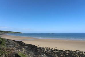 A coastal beach with a rocky shoreline, clear blue sky, and calm sea. - Tritons Retreat, Sir Ynys Mon. (Moelfre)