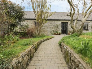 A stone building with a paved pathway leading to a black door. - Brunnion Cottage, St Ives (Hayle)