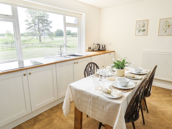Un comedor con una mesa lista para cuatro personas, una ventana que ofrece vistas a un árbol y césped, y un radiador en la pared.
