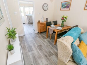 A cozy living room with a sofa, a dining table with chairs, a kitchen in the background, and a clock on the wall. - Cranford Cottage: Cozy Retreat (Pembroke)
