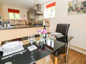 A dining table set with plates, glasses, and a vase of flowers in a modern kitchen with a stove, microwave, and cabinets. - Charming The Lodge in Disley (Stockport)