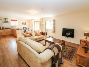 A living room with a sofa, a coffee table, a TV, and a kitchen area with cabinets and a stove.