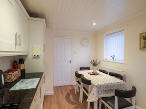 A compact kitchen with a dining table, chairs, a clock, and a window with blinds.