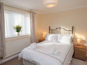 A neatly made bed with white linens, a bedside lamp, and a window with curtains.