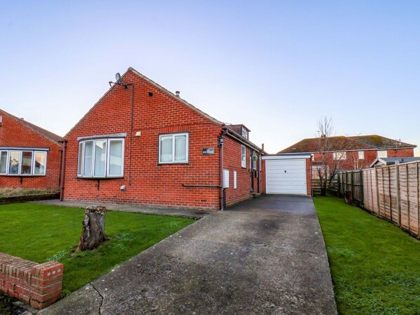 A red brick house with a garage, a paved driveway, and a well-maintained lawn.