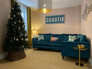 Ein Wohnzimmer mit Weihnachtsbaum, einem türkisblauen Sofa und einem 'COASTIE'-Schild an der Wand.