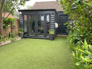 Ein Garten mit einer kleinen Terrasse, einer Glastür und Kübelpflanzen.