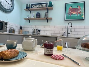 Eine Küche mit einer Uhr, einem 'Champagne'-Schild, einem Marmeladenglas, einem Teekessel, einem Croissant und einem Glas Orangensaft.