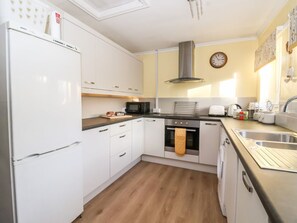 A kitchen with white cabinets, a Bosch refrigerator, a microwave, an oven, a sink, and a clock on the wall. - Millers Cottage in Old Malton. (Malton)