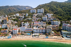Un paysage urbain côtier avec une plage, de grands hôtels et, en arrière-plan, des collines verdoyantes.