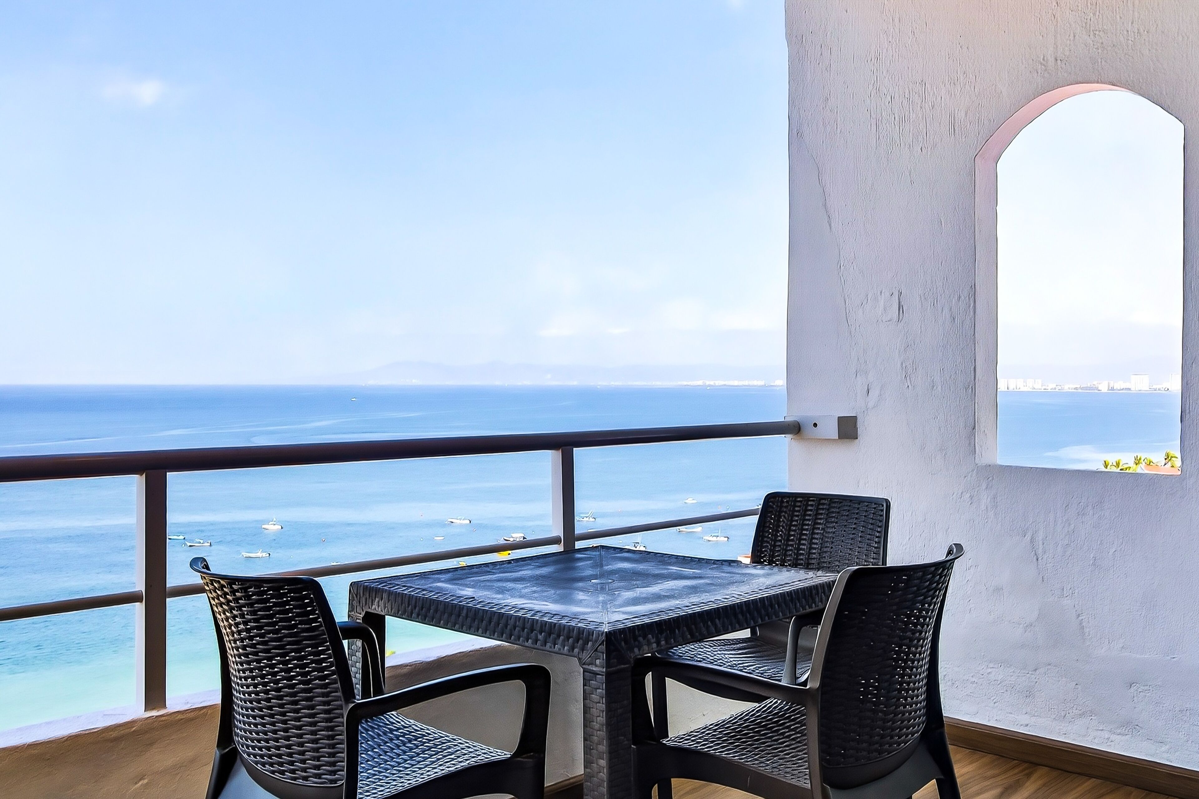 A balcony with a table and chairs, overlooking the sea with boats in the distance.