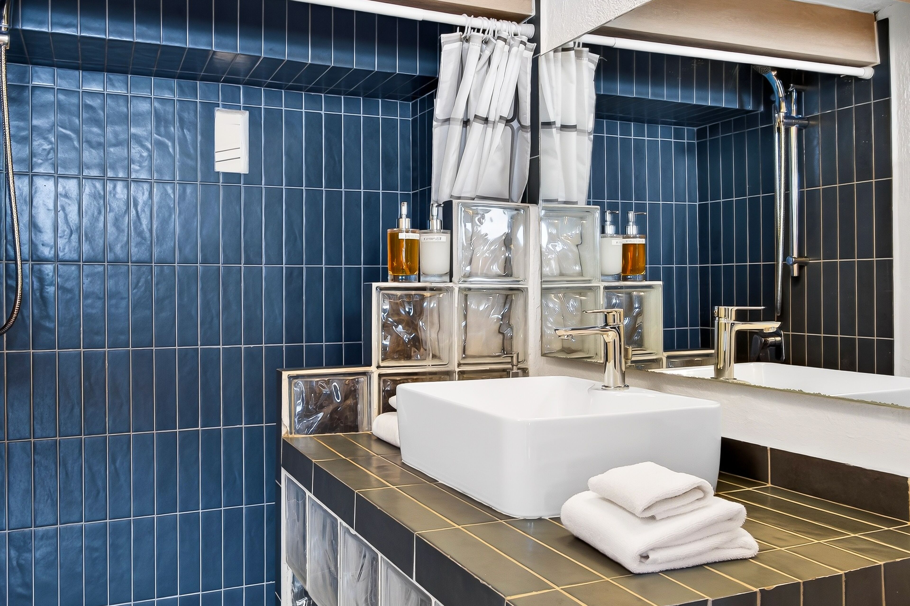 Un baño moderno con azulejos azules, una bañera blanca, un espejo grande y una zona de ducha.