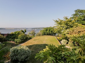 A well-maintained garden with a lawn and various shrubs, leading to a body of water with boats. - Riverview @ 1 Brunel View 1bed (Saltash)