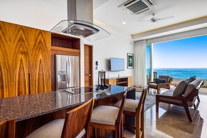 A modern kitchen with a granite countertop, wooden cabinetry, and a built-in oven. There is a dining area with a bar and seating, and a large window offering a view of the ocean. - Blue Horizon 502 | 1BR/2BA Puerto Vallarta Ocean View, Pool & Gym (Puerto Vallarta)