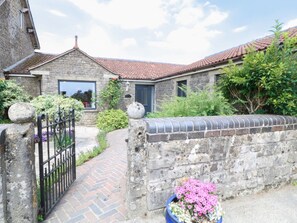 A stone building with a red-tiled roof, a brick pathway, and a garden with flowers. - Leigh Holt, Shepton Mallet (Shepton Mallet)