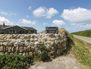 Eine Steinsäule mit einem Schild, das 'Boscastle View' zeigt, und ein Haus im Hintergrund.