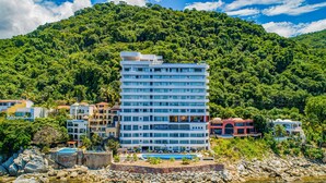 Un hotel a più piani con piscina, immerso nel verde rigoglioso e affacciato su una costa rocciosa.