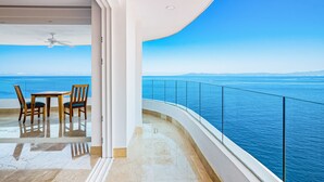 Un balcone con ringhiera in vetro che si affaccia su una distesa d'acqua, un tavolo con sedie e una ventola a soffitto.