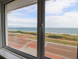 Blick durch ein Fenster auf eine Küstenstra ße mit Strand und Meer im Hintergrund.