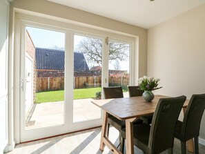 A room with a sliding glass door leading to a backyard, a wooden table with chairs, and a vase with flowers. - Sunnyside, Wells-Next-The-Sea (Wells-next-the-Sea)