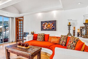 A modern living room with a curved orange sofa, a wooden coffee table, and a large window with a view of the city. - Downtown Malecon beach front, AC, walk to restaurant/bars, rooftop 360 views (Puerto Vallarta)