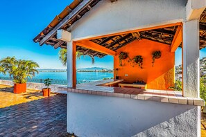 A covered outdoor seating area with a view of the sea, potted plants, and a tiled floor. - Downtown Malecon beach front, AC, walk to restaurant/bars, rooftop 360 views (Puerto Vallarta)