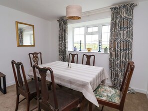 Ein Esszimmer mit Tisch für vier Personen, einem Spiegel an der Wand und gemusterten Vorhängen.