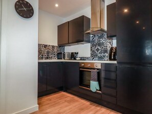 Een moderne keuken met donkere kasten, een roestvrijstalen afzuigkap, een decoratieve spatwand en een klok aan de muur.