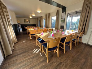 Ein Essbereich mit Holztischen und -stühlen, einem Buffet und großen Fenstern mit Vorhängen.