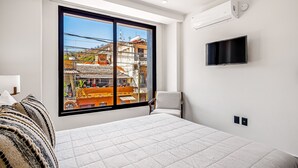 Ein modernes Schlafzimmer mit großem Fenster, einem Bett, einem Sessel und einem an der Wand befestigten Fernseher.
