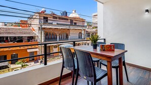 Ein Balkon mit einem Holztisch und Stühlen, einem Blumentopf und einer Spielebox.