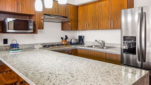 Eine moderne Küche mit Granit-Arbeitsplatten, Edelstahlgeräten, Holzschränken und Pendelleuchten.