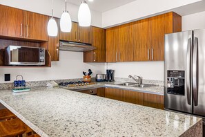 A modern kitchen with granite countertops, stainless steel appliances, wooden cabinets, and pendant lighting. - 2BR Serenity Condos #201 in PV near ocean, pool, BBQ (Puerto Vallarta)