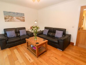 A living room with two black leather sofas, a wooden coffee table with a vase of flowers, and a painting on the wall. - Cherry Tree House, Penzance (Penzance)