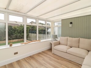 A conservatory with a sofa and a lamp, large windows, and a view of a garden. - Gudhjem, Seahouses, Sleeps ten (Seahouses)